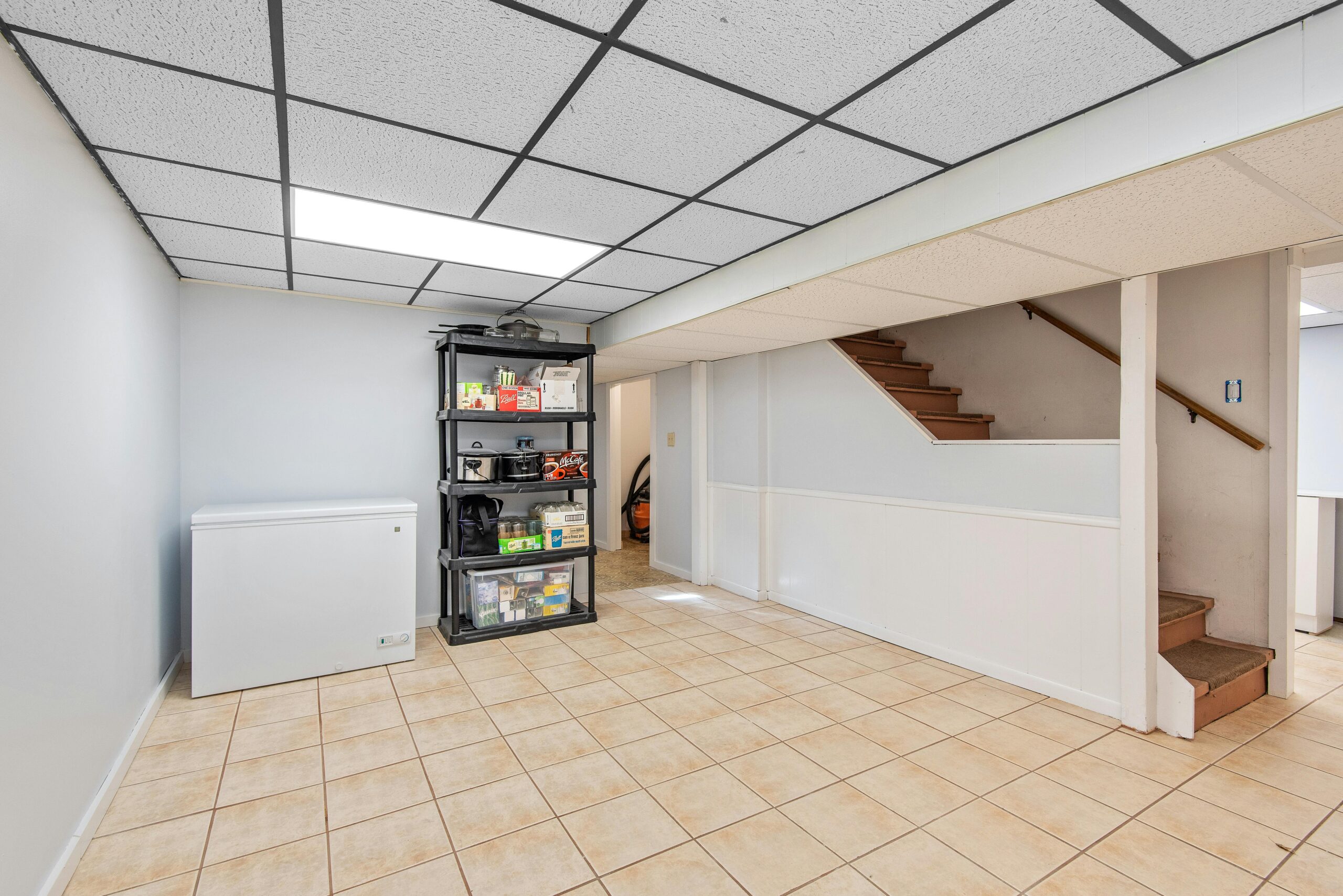 Spacious basement featuring tiled floor, storage shelves, and staircase in a modern setting.