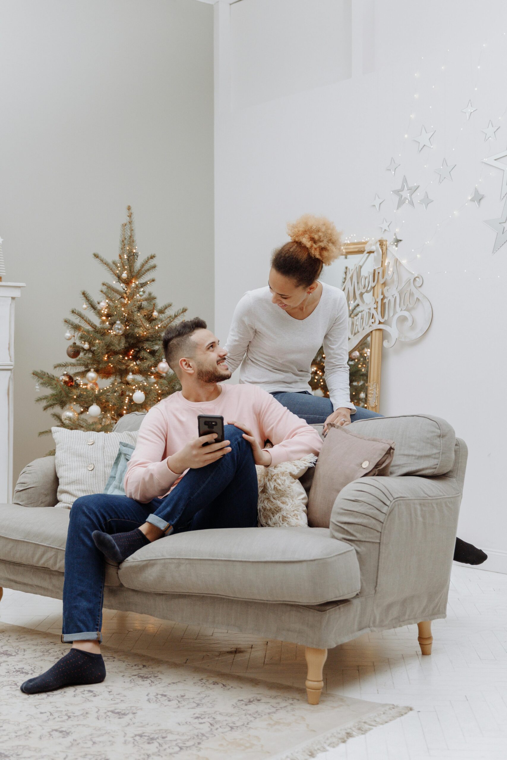 A happy couple sitting on a sofa, enjoying a cozy Christmas setting at home.